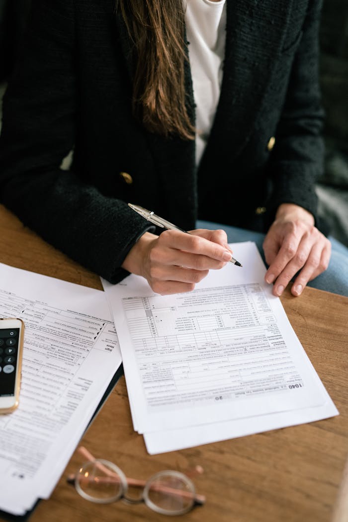 Close-up of a person reviewing and signing documents at a wooden desk, business attire.