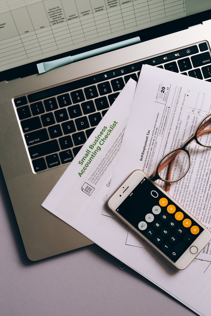 Small business accounting setup featuring a laptop, documents, and smartphone calculator.
